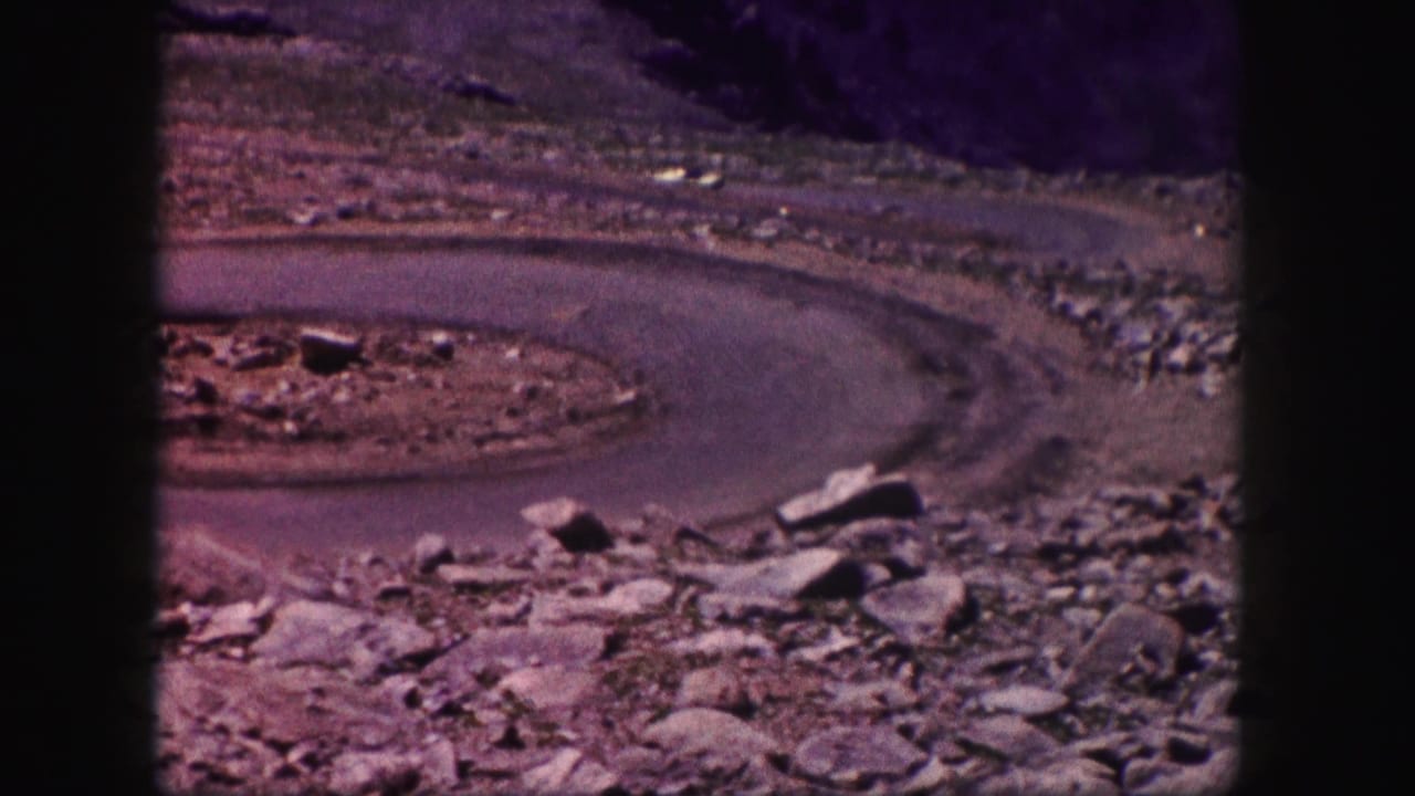 A curved paved road passes through rocky ground with a small distant car near the bend.