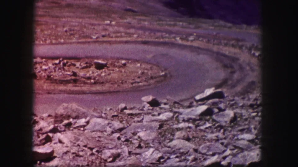 1958 Colorado home-movie frame of a paved road looping through rocky desert terrain, with no people or signage visible.