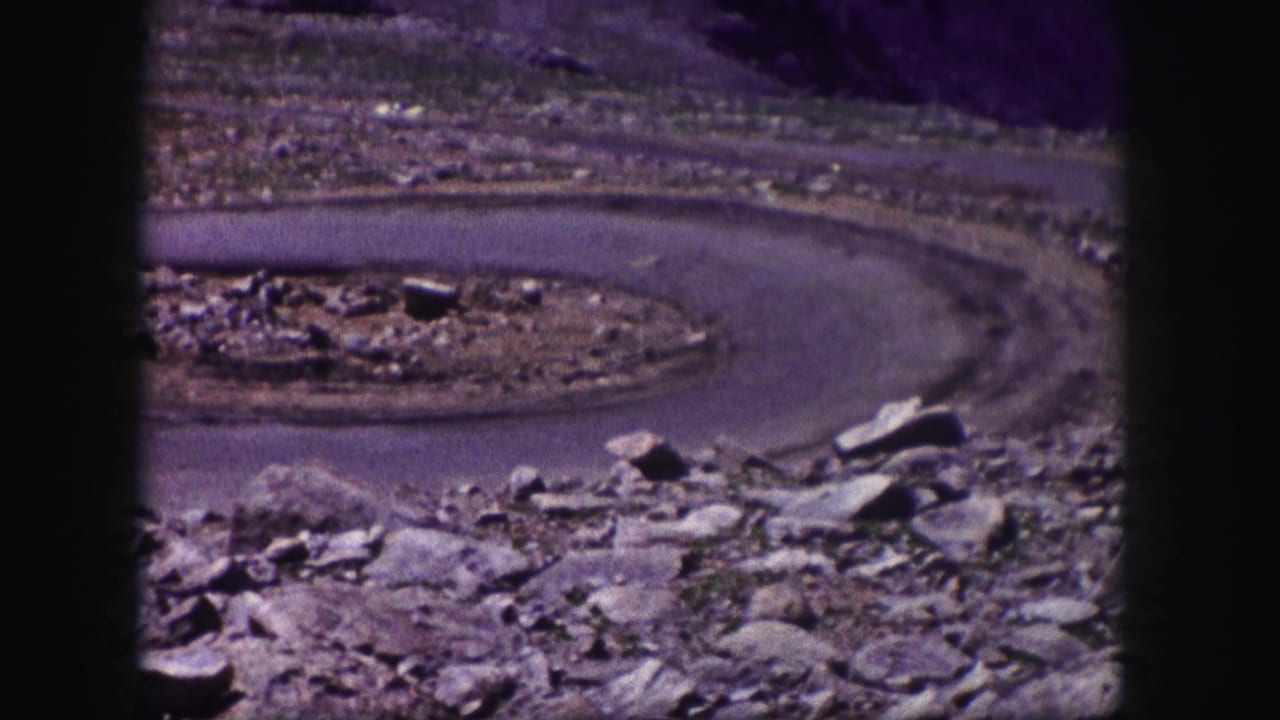 1958 Colorado 8mm frame showing a winding mountain road seen from a rocky overlook, with barren slopes and distant terrain.