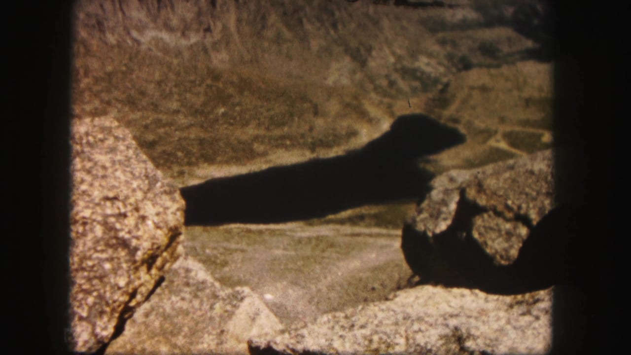 Sunlit rocky ground with a long dark shadow across mountain terrain.