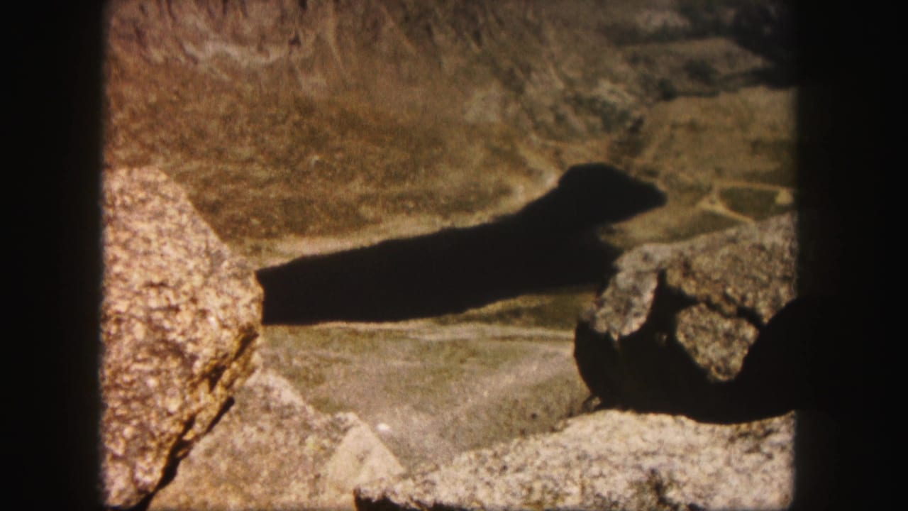 1958 Colorado home-movie view of a dark shadow crossing sunlit rocky terrain near the end of a hike.