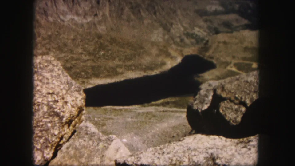 Final 1958 Colorado hiking frame with a long shadow over rocks and brown mountain terrain inside 8mm borders.