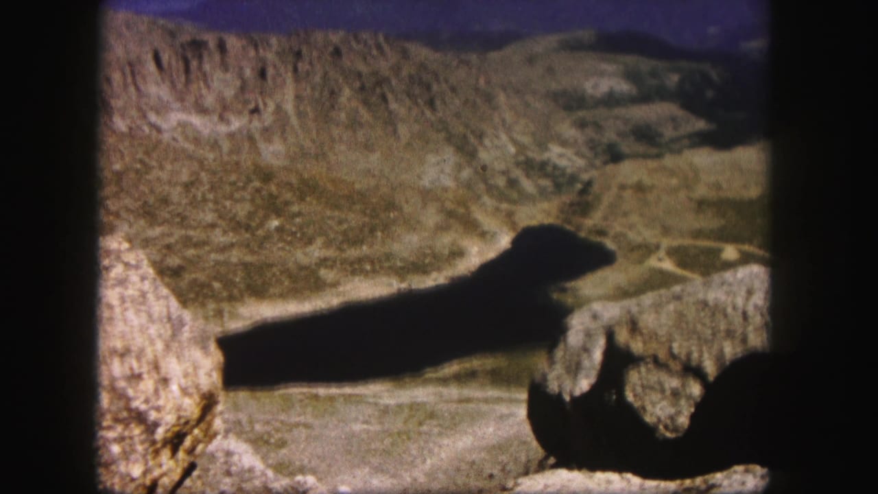 Mountain valley view with dark water and foreground rocks.
