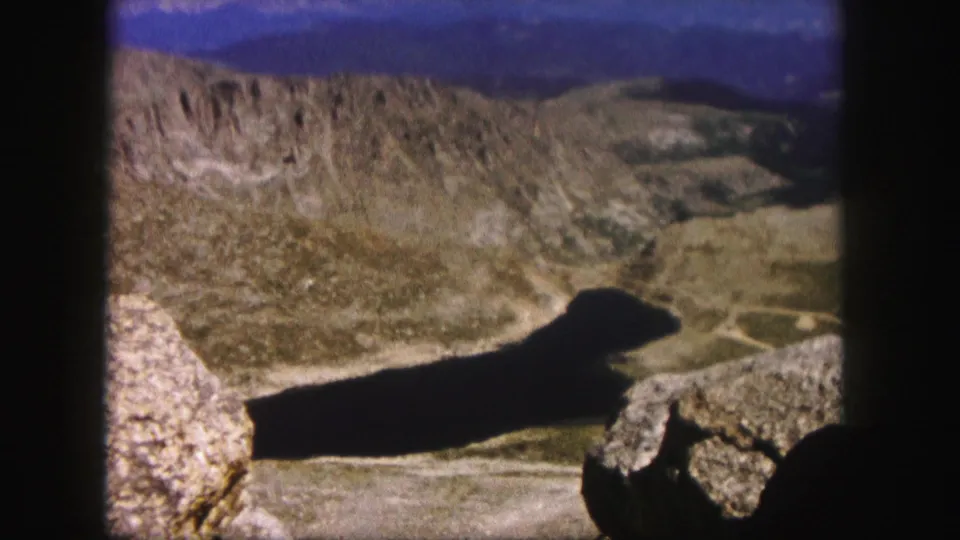 Colorado 1958 8mm landscape frame showing a shadowed body of water below dry mountain slopes from a high rocky viewpoint.
