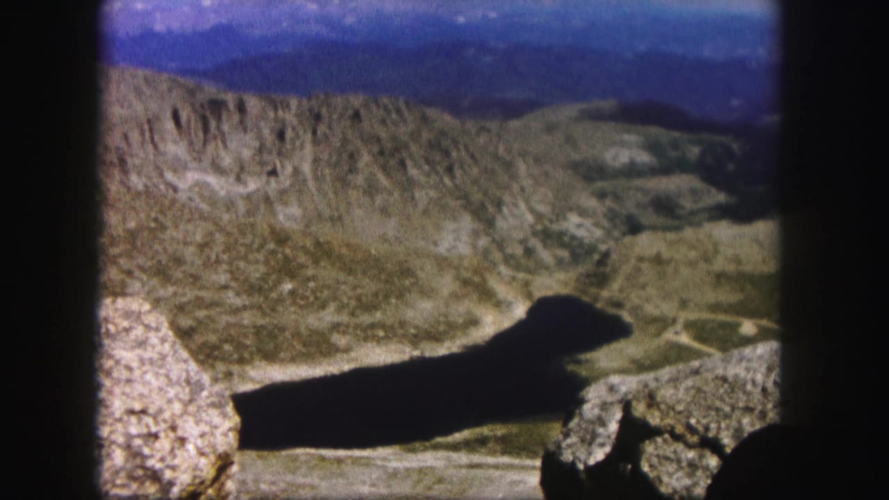 1958 Colorado home-movie view across rocky terrain toward a dark alpine lake and distant ridges.
