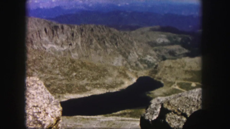 1958 Colorado home-movie view across rocky terrain toward a dark alpine lake and distant ridges.