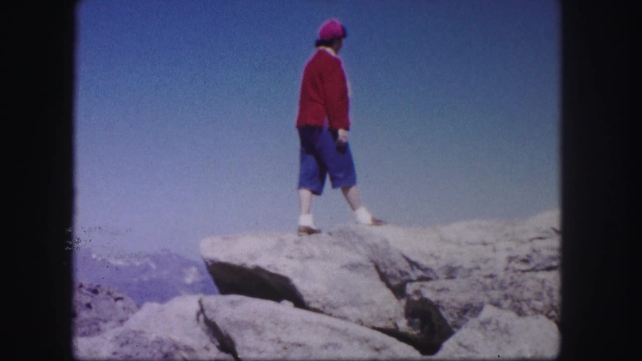 Woman in red sweater and blue pants standing on a rocky ledge.