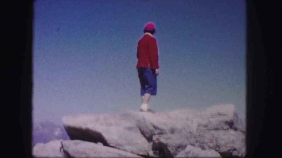 Rear view of a woman standing on a pale mountain rock ledge in 1958 Colorado home-movie footage.