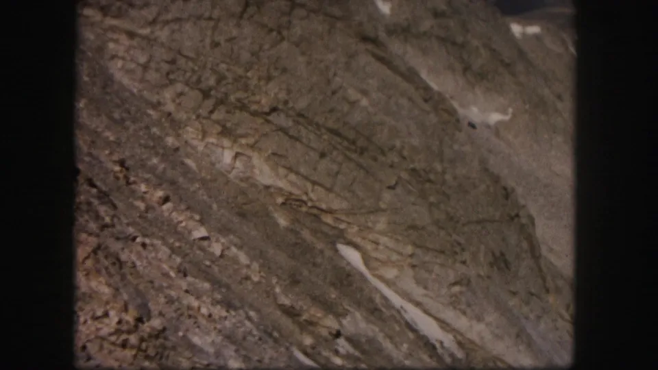 Close 8mm view of Colorado mountain rock, showing diagonal strata, loose scree, and small remnants of snow.