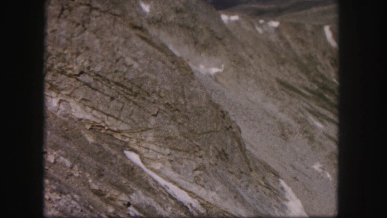 1958 Colorado 8mm frame showing bare rocky mountain terrain with scattered snow patches and soft grain.