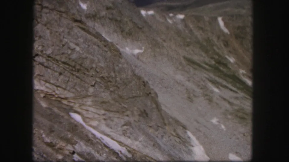 1958 Colorado home-movie frame of rugged bare mountain terrain, pale snow streaks, and muted 8mm color.