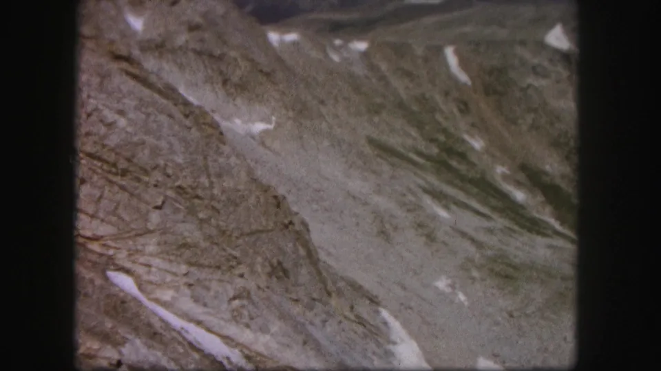 1958 Colorado 8mm frame showing a steep rocky slope crossed by diagonal snow patches and grainy color texture.
