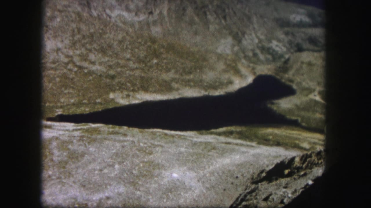 Rocky mountain valley with a long dark shadow across the pale ground.