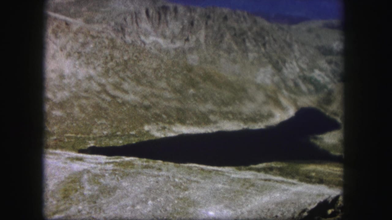 Dark shadow across a rocky valley beneath steep mountain slopes.