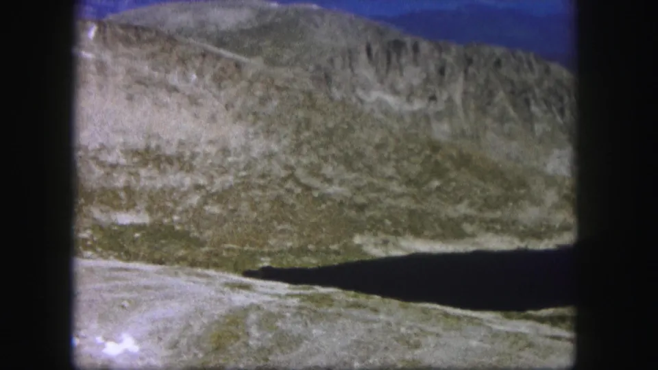 1958 Colorado 8mm view of rocky slopes and dry valley ground as the shadowed foreground moves toward the edge of the frame.