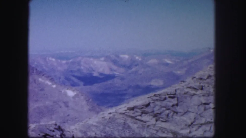1958 Colorado 8mm frame showing a rocky high ridge and hazy distant mountain ranges with small snow patches.