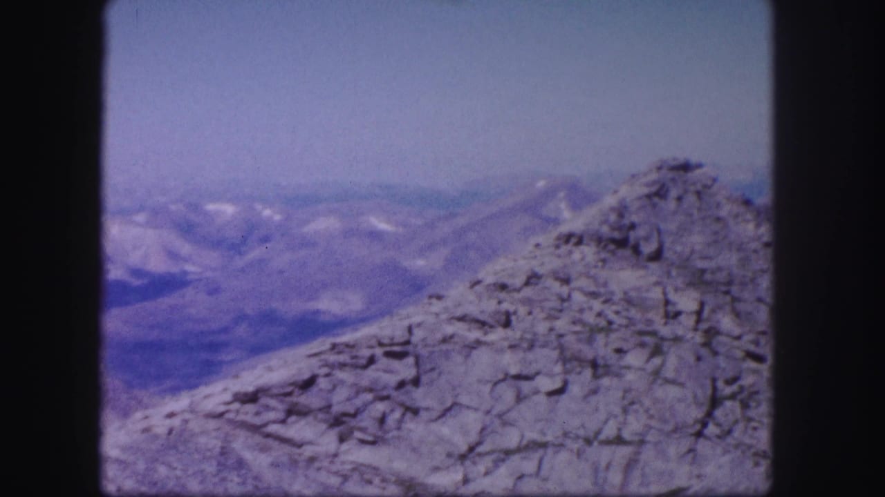 Rocky peak at right with distant mountain ridges and patches of snow.