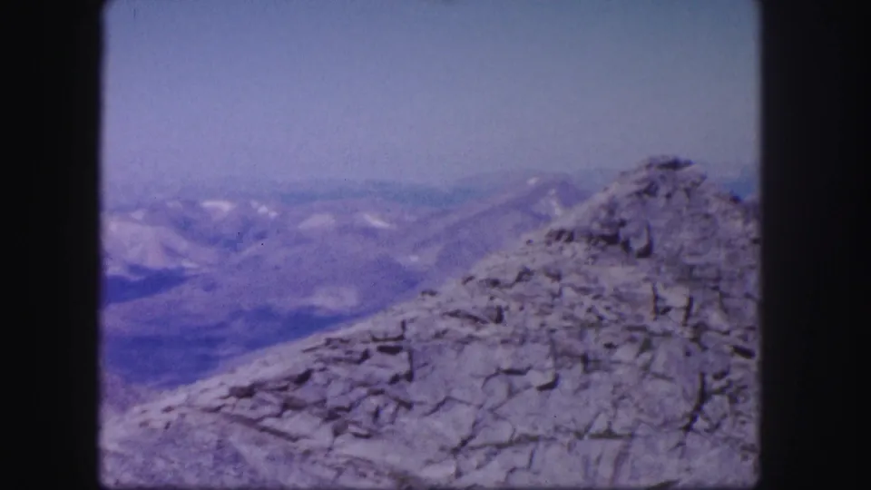 Colorado mountain panorama on aged 8mm film, with a rough rocky peak in the foreground and hazy ranges beyond.