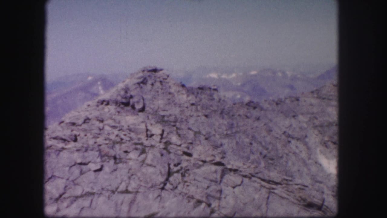 Rocky mountain foreground with hazy distant ridges and snow patches beyond.