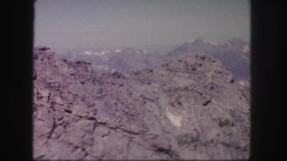 1958 Colorado 8mm still showing a weathered rocky slope, muted mountain ridges, and scattered snow patches beyond.