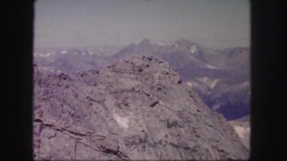 1958 Colorado 8mm frame of a rocky foreground ridge, distant alpine peaks, haze, and dark scan borders.