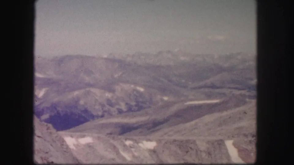 1958 Colorado 8mm frame looking across open mountain ridges, shadowed valleys, pale sky, and lingering snow patches.