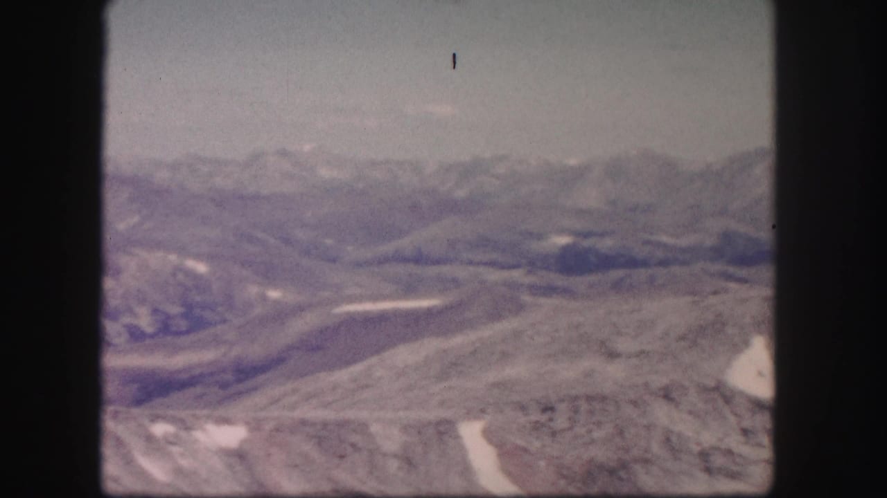 1958 Colorado home-movie frame of layered mountain ridges and barren rocky terrain, softly exposed on 8mm film.