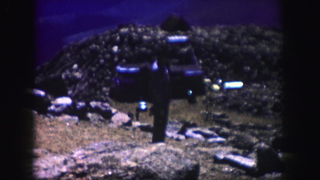 Solitary figure stands on rocky ground beneath a dark blue-purple sky.