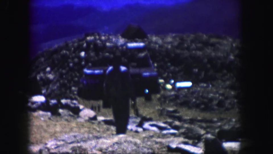 Grainy 8mm frame from Colorado showing a lone person in a rocky landscape with visible gate edges and color shift.
