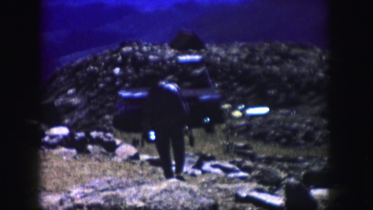 A man in dark clothing moves through a rocky Colorado landscape near a parked car in 1958 8mm home-movie footage.