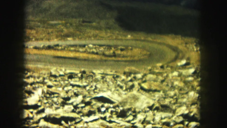 A winding road cuts through a rocky Colorado landscape, seen in grainy 1958 8mm color home-movie footage.