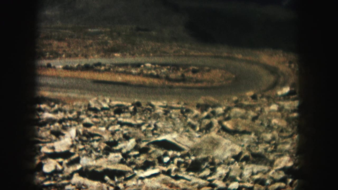 Curving road and rocky foreground framed by dark film edges.