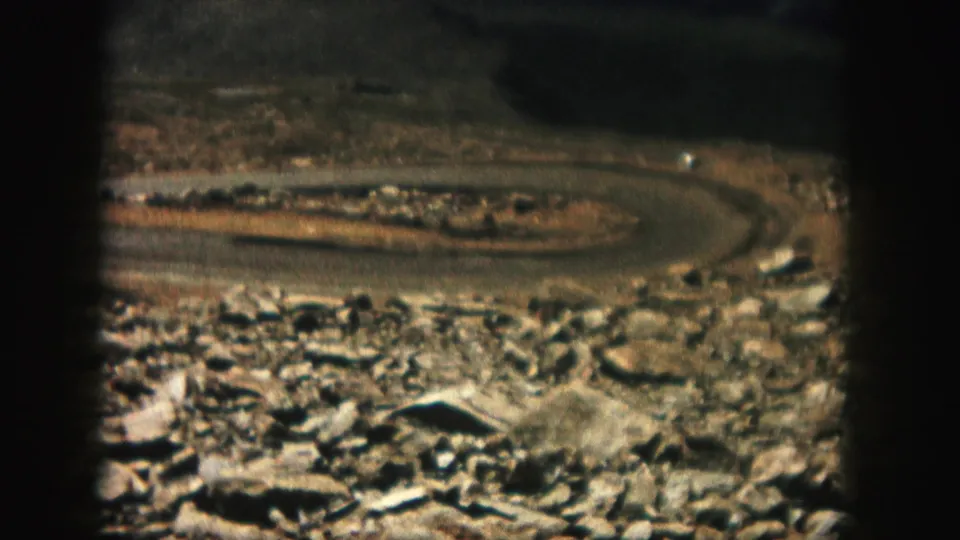 1958 Colorado 8mm still of a winding road crossing a rocky, arid landscape under muted light.