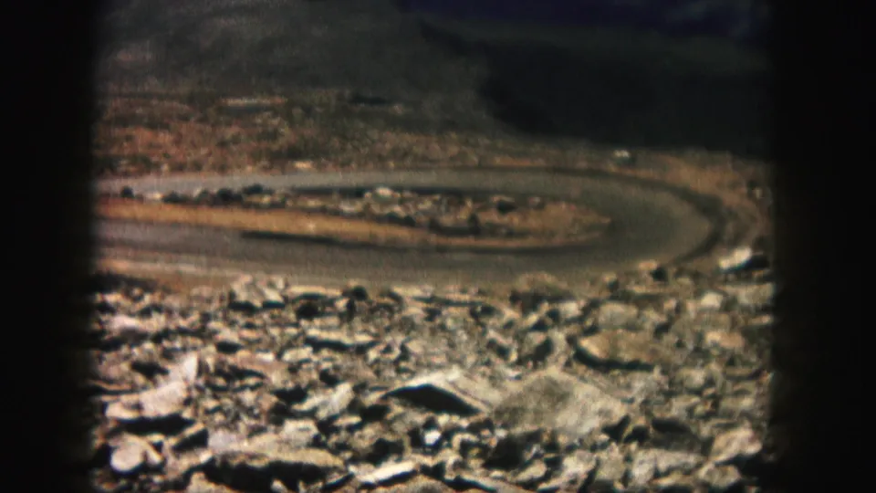 1958 Colorado 8mm frame showing a U-shaped road behind a rocky foreground and sparse roadside vegetation.