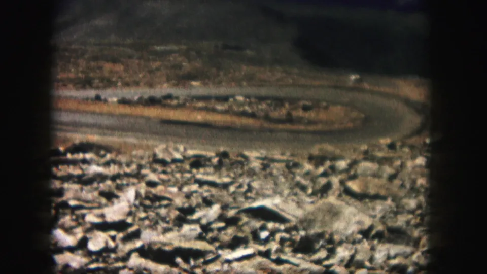 1958 Colorado home-movie frame with a curved road across rocky terrain and visible dark 8mm frame borders.