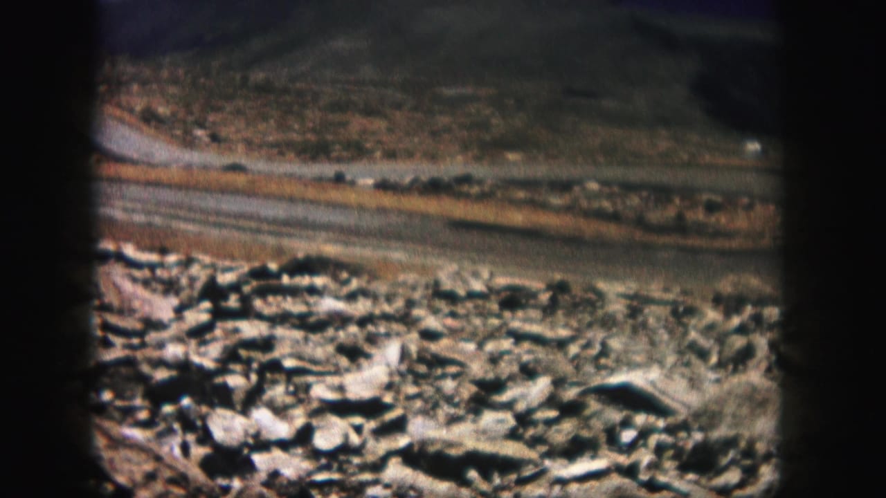 Rocky slope and narrow road seen through dark 8mm film frame edges.