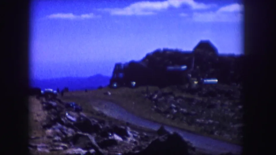 Final 1958 Colorado frame showing the same blue-tinted mountain road scene with rocky foreground and a distant structure on the hillside.