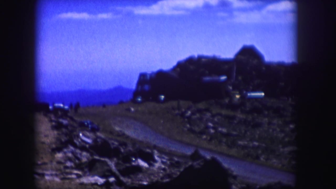 Rocky dirt road curving toward a dark structure under a blue sky.