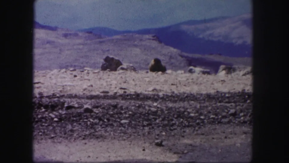 1958 Colorado home-movie view across a rocky foreground toward pale arid flats, boulders, and distant mountain slopes.