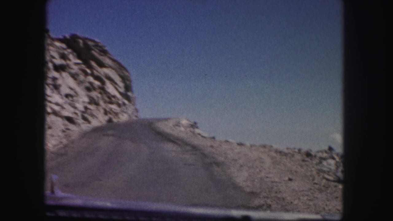 First-person 8mm Colorado road view with a rock face on the left and the vehicle hood at the bottom.