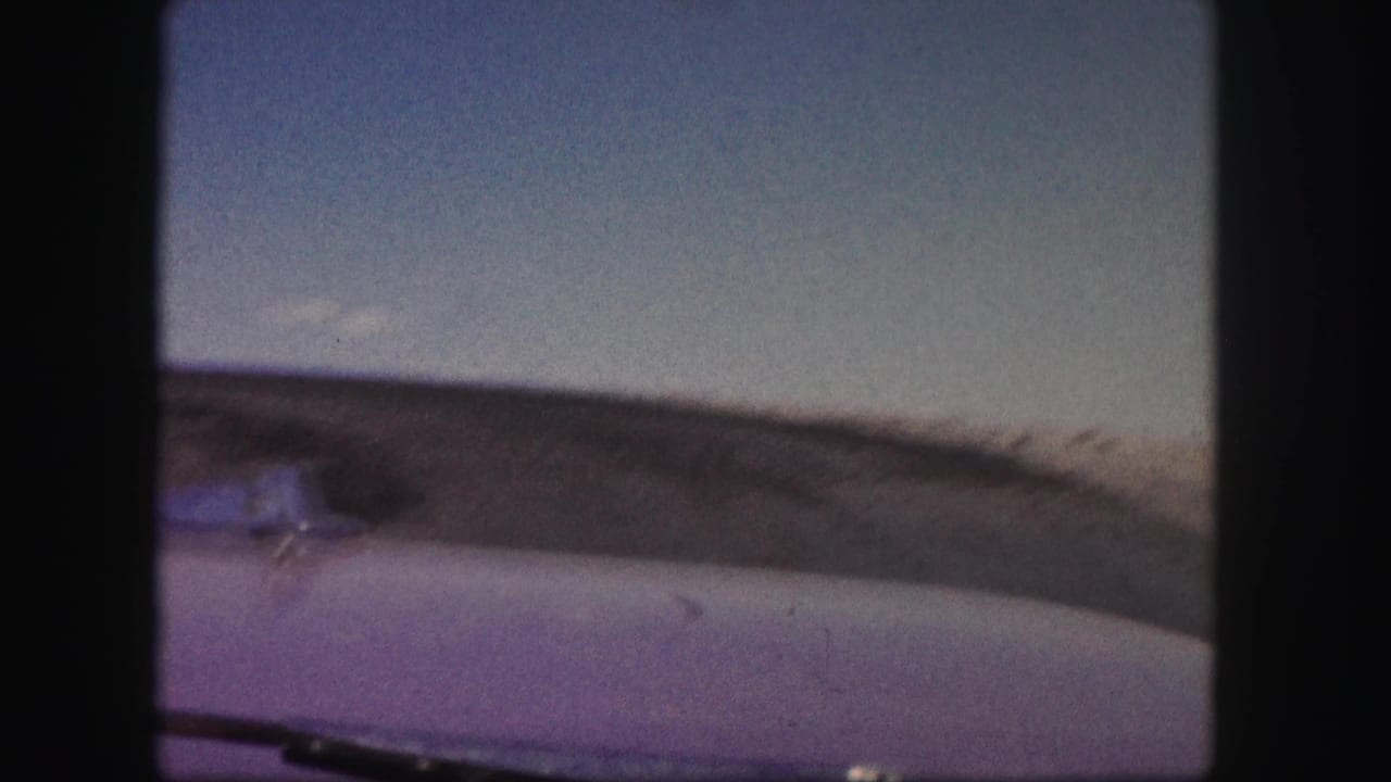Windshield view across a car hood toward a low brown hill and open blue sky.