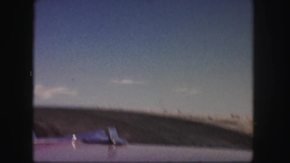 Colorado driving POV on 8mm film, with a purple hood, small dashboard objects, distant hillside, and pale blue sky.