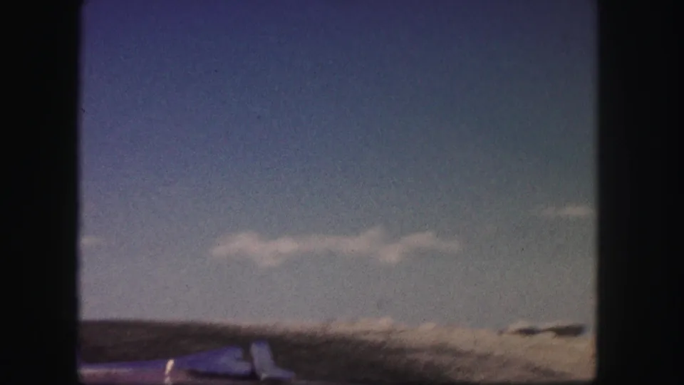 1958 Colorado road-trip view with blue sky, scattered clouds, distant arid hills, and the car hood at the bottom edge.
