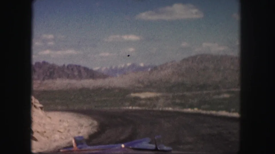 A winding Colorado mountain road curves through rugged terrain under scattered clouds in this 1958 8mm frame.