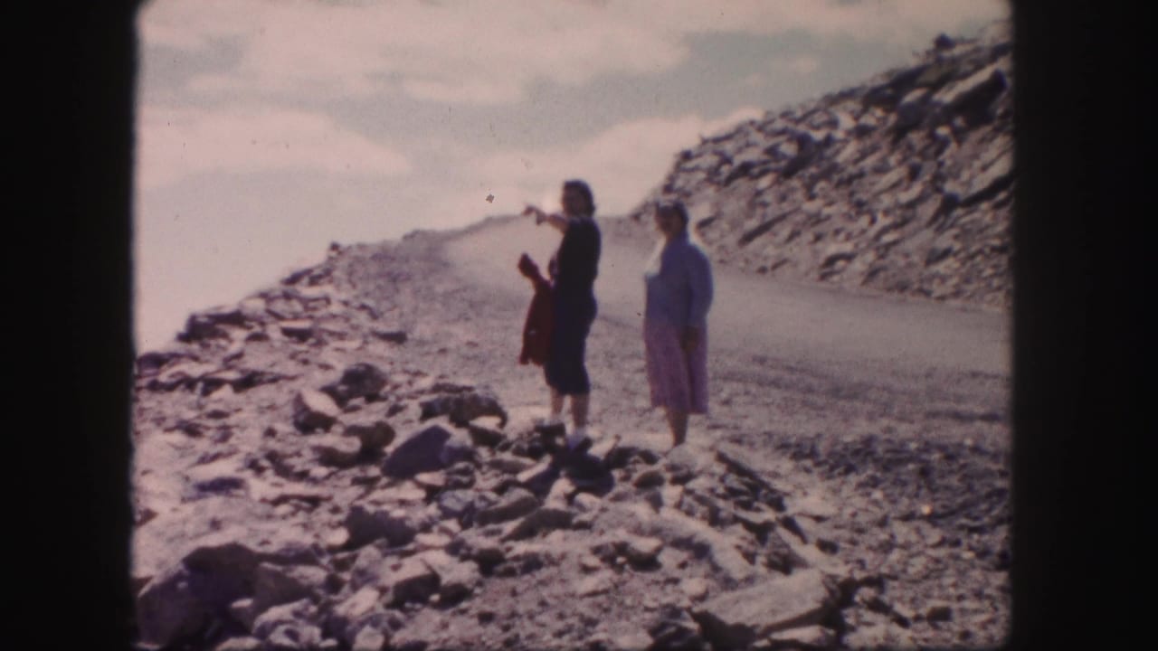 Two women stand on a rocky mountain road in Colorado, one holding a red garment and looking toward the distant view.