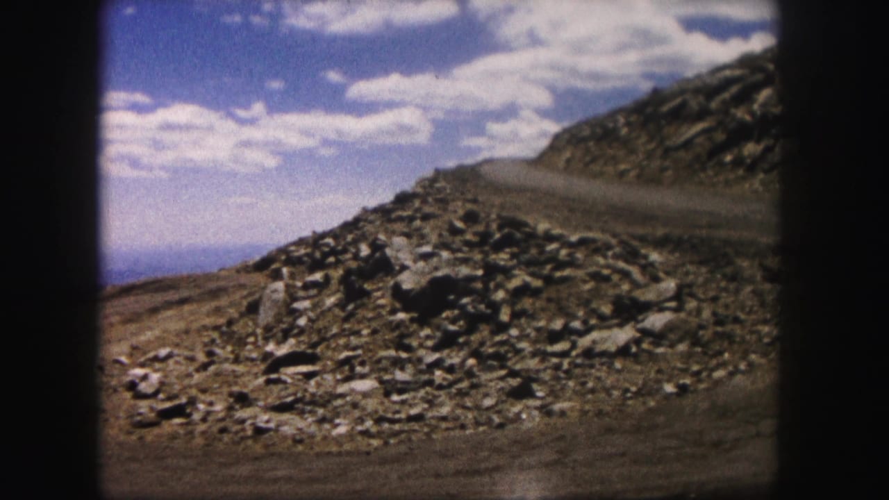 Rock-strewn slope and road edge with clouds over a distant blue horizon.