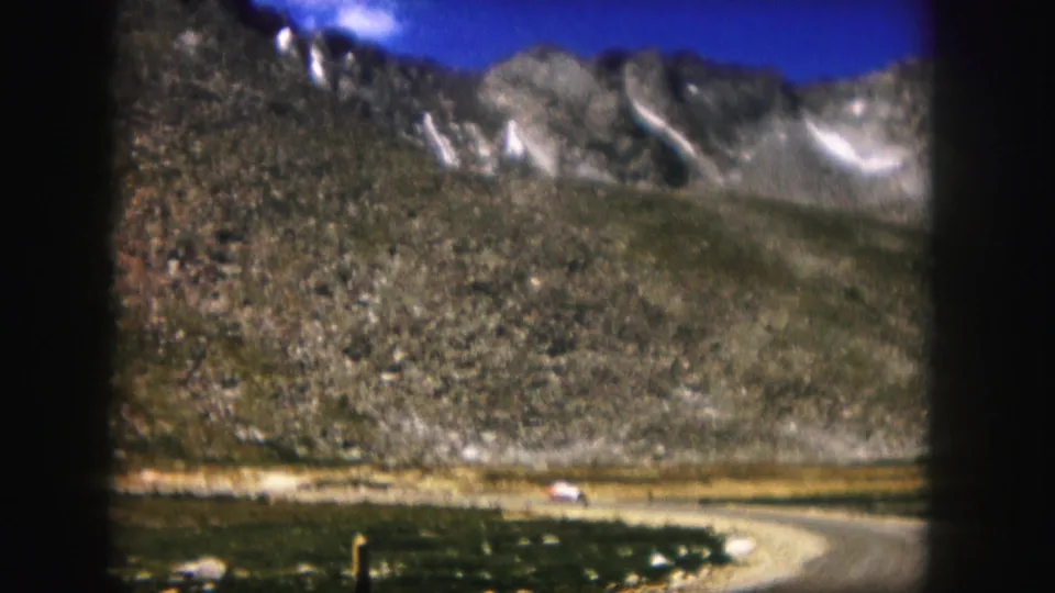 1958 Colorado 8mm view of a distant car on a curved mountain road, framed by grain and dark film edges.