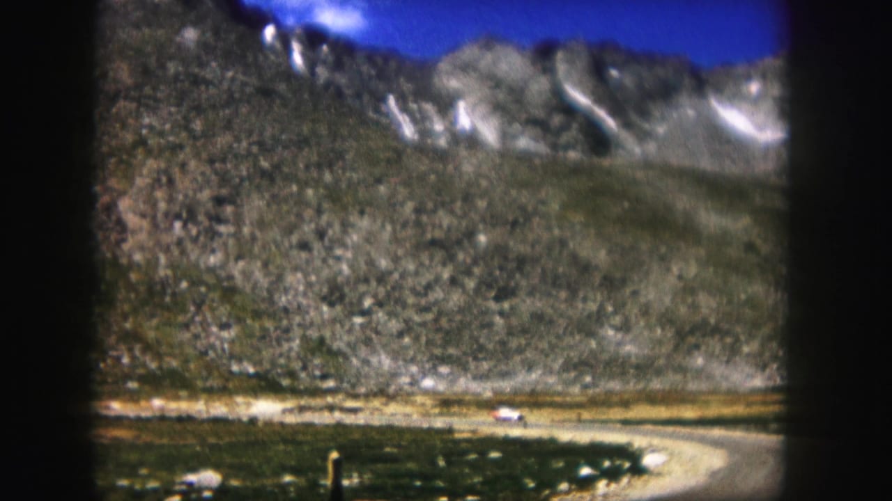 1958 Colorado 8mm frame showing a rocky mountain valley, winding road, distant peaks, and a small light-colored vehicle.