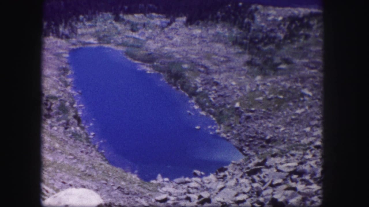 Blue alpine lake surrounded by rocks and scrub on a mountain slope.