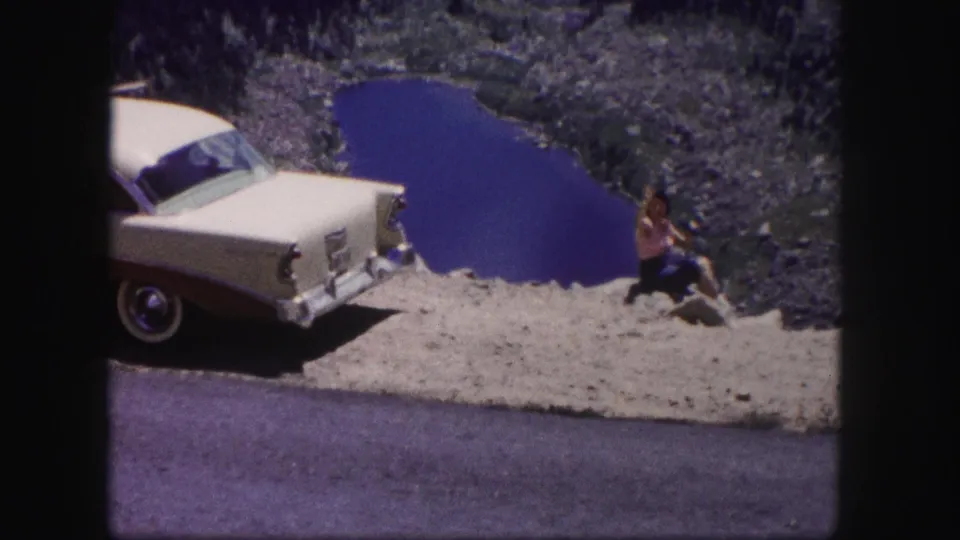 The final frame shows the woman seated near a roadside overlook, with the two-tone sedan and Colorado lake behind her.
